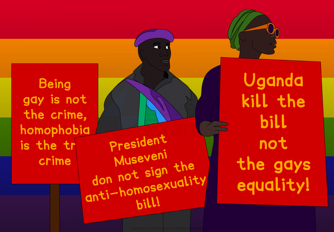 Protesters holding red signs with anti-homophobia messages including "Being gay is not the crime," and "Kill the bill, not the gays," with rainbow flags.