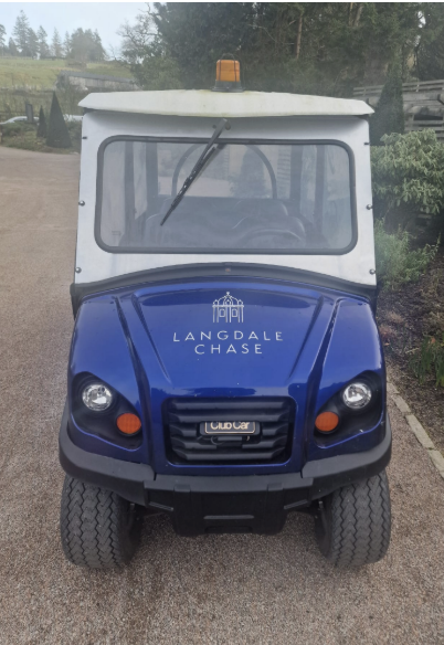 Electric utility vehicle with "Langdale Chase" branding on the bonnet, parked on a gravel path with greenery and trees in the background.