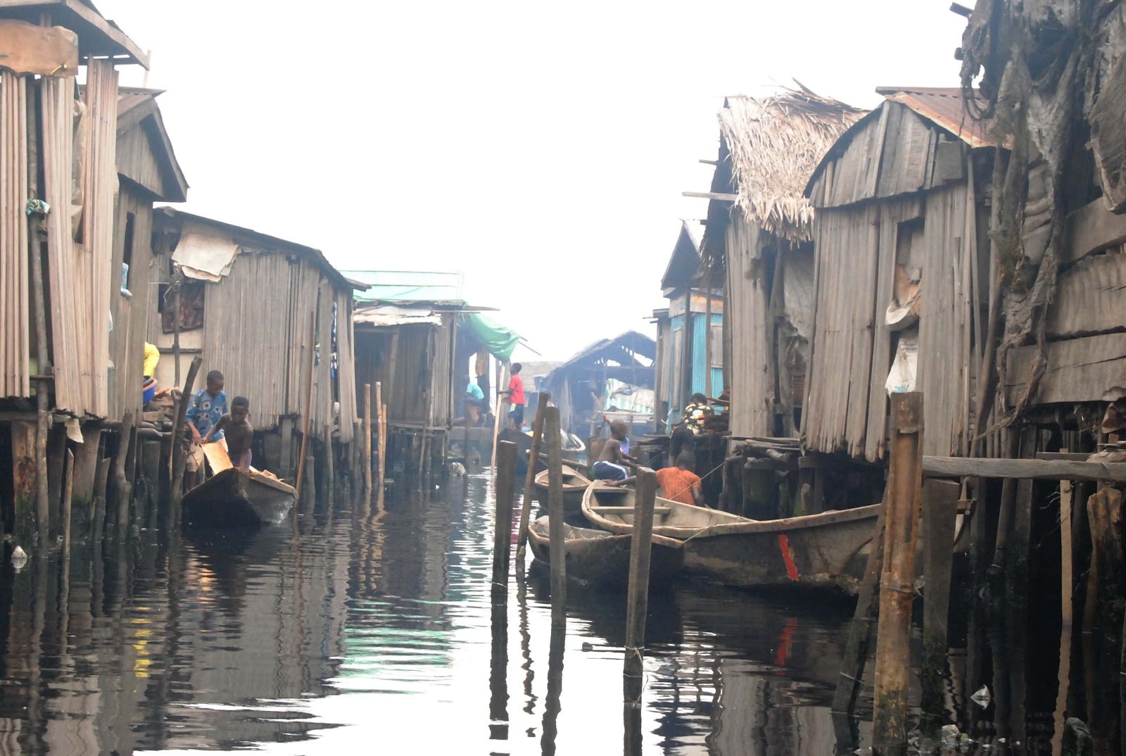 Stilt houses over water in a densely populated area, with wooden canoes being paddled by locals through narrow water channels.