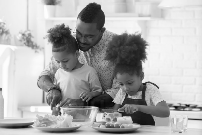 Father and two children cooking together in a bright kitchen, focusing on chopping vegetables on a countertop, surrounded by kitchenware.