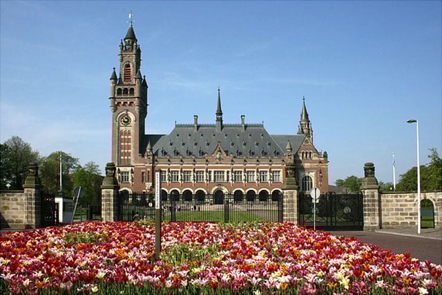 Historic building with a clock tower, surrounded by a manicured garden full of colourful tulips, under a clear blue sky.