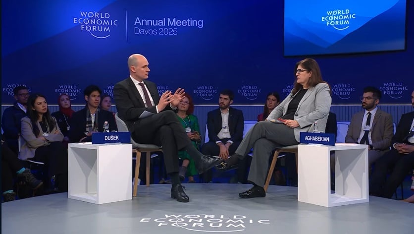 Two individuals engaged in a discussion on stage at the World Economic Forum 2025 in Davos, surrounded by an audience with forum branding visible.