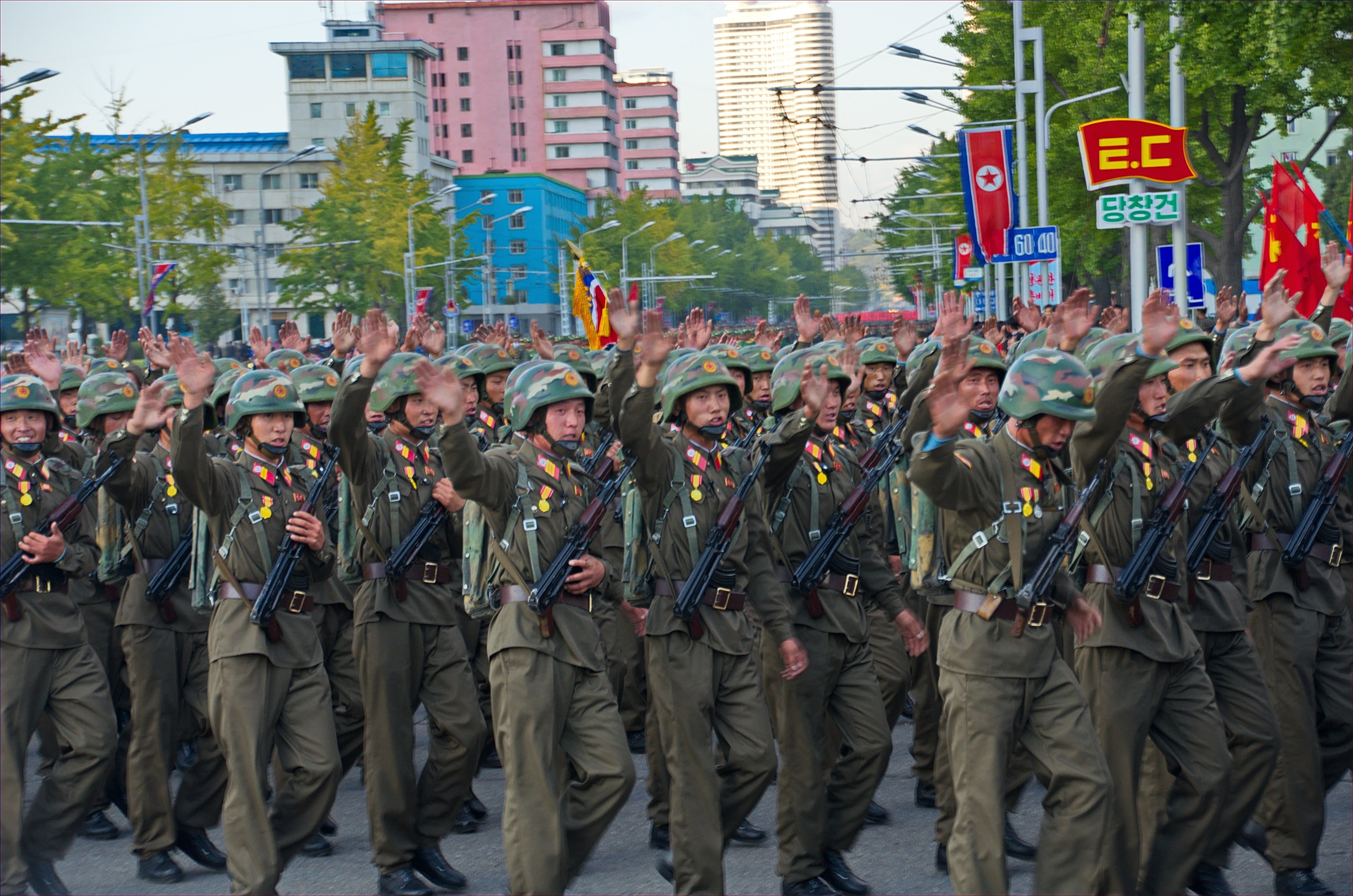 A parade of waving soldiers in North Korea, with the national flag in the background