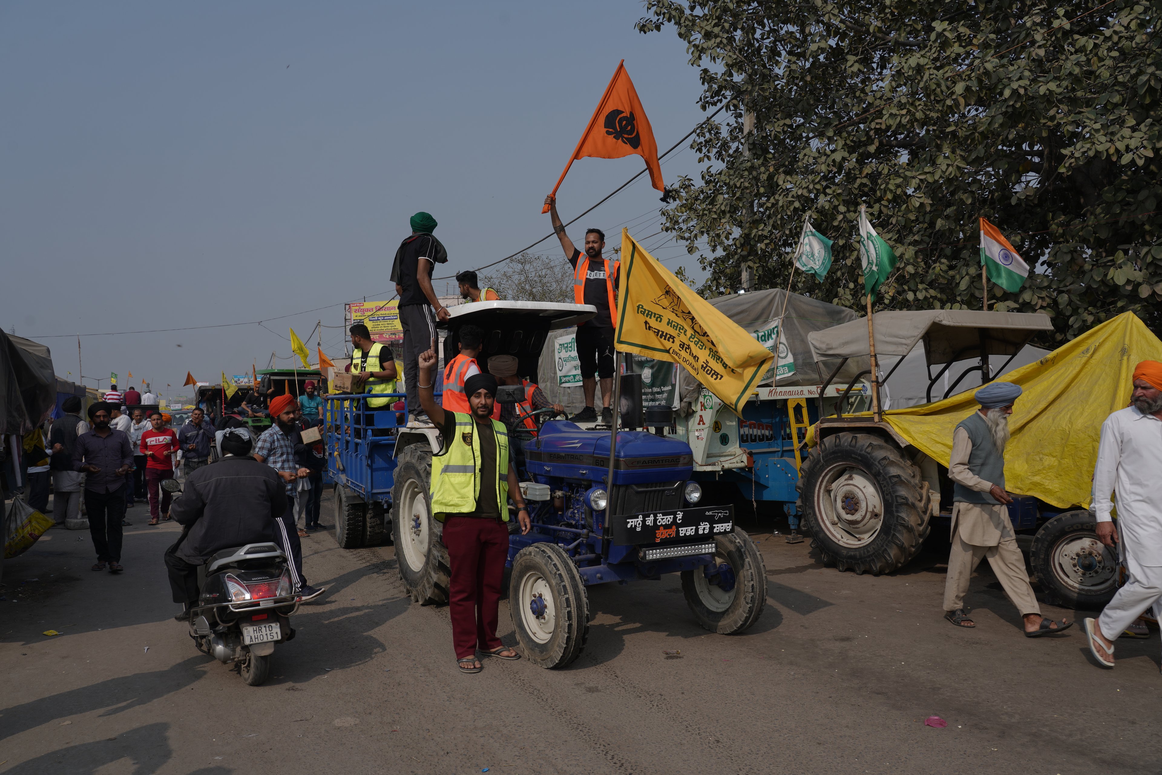 A procession of farm vehicles block a busy road in India, with supporters alongside and trade union flags