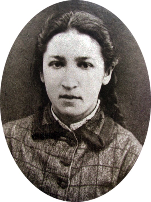 Old black-and-white oval portrait of a young woman facing the camera, wearing a checked high-collared dress with braided hair pulled back