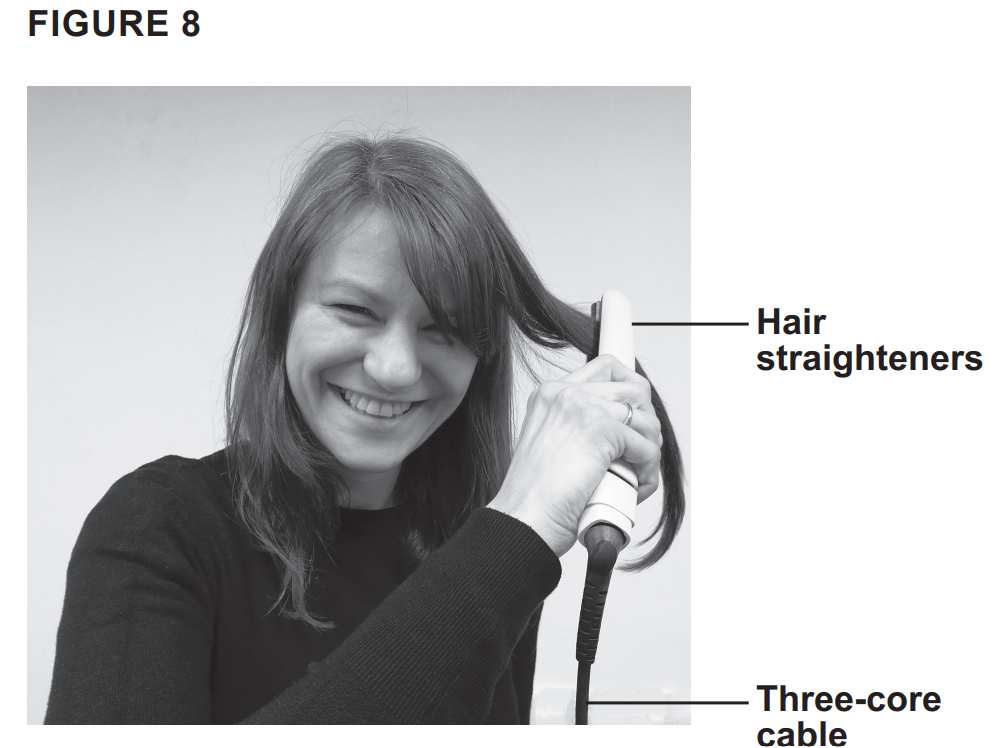 Smiling woman using electric hair straighteners on her hair, with labelled arrows pointing to the straighteners and their three-core cable