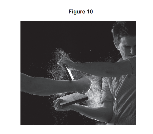 Black-and-white photo of a man blocking an arm strike with a forearm and padded board, white powder exploding on impact against a dark background