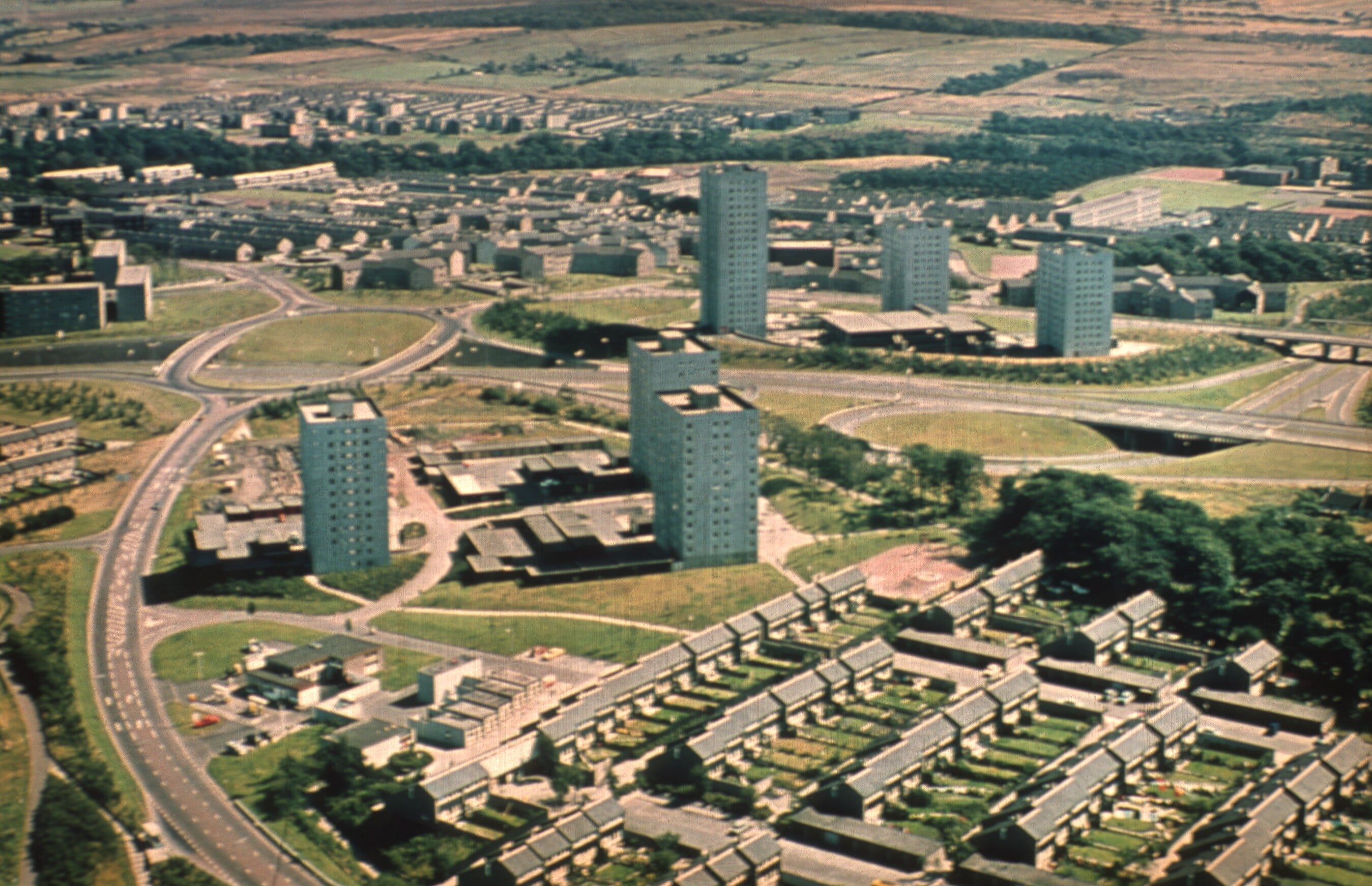Aerial view of a 1960s housing estate with tall tower blocks, low terraced houses, dual carriageways and roundabouts amid green open spaces