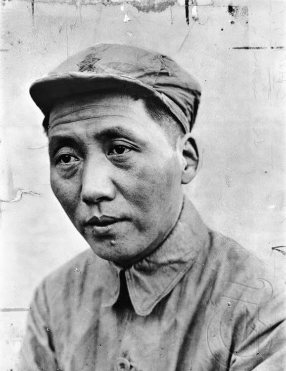 Black-and-white portrait of an unsmiling man in a military-style cap and buttoned uniform, looking slightly downwards against a plain, worn backdrop