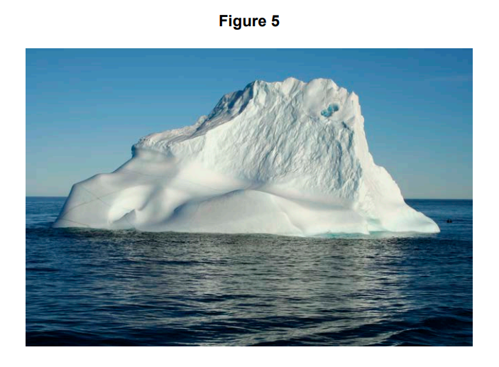 Large white iceberg floating in calm, dark blue sea under a clear sky, showing smooth and jagged ice surfaces in bright sunlight