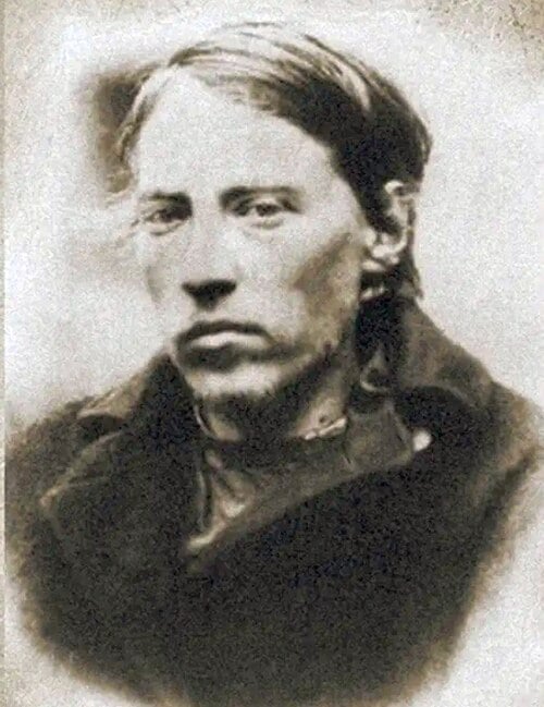 Faded vintage portrait of a solemn young man with tousled hair and coat, facing the camera against a plain, softly blurred background
