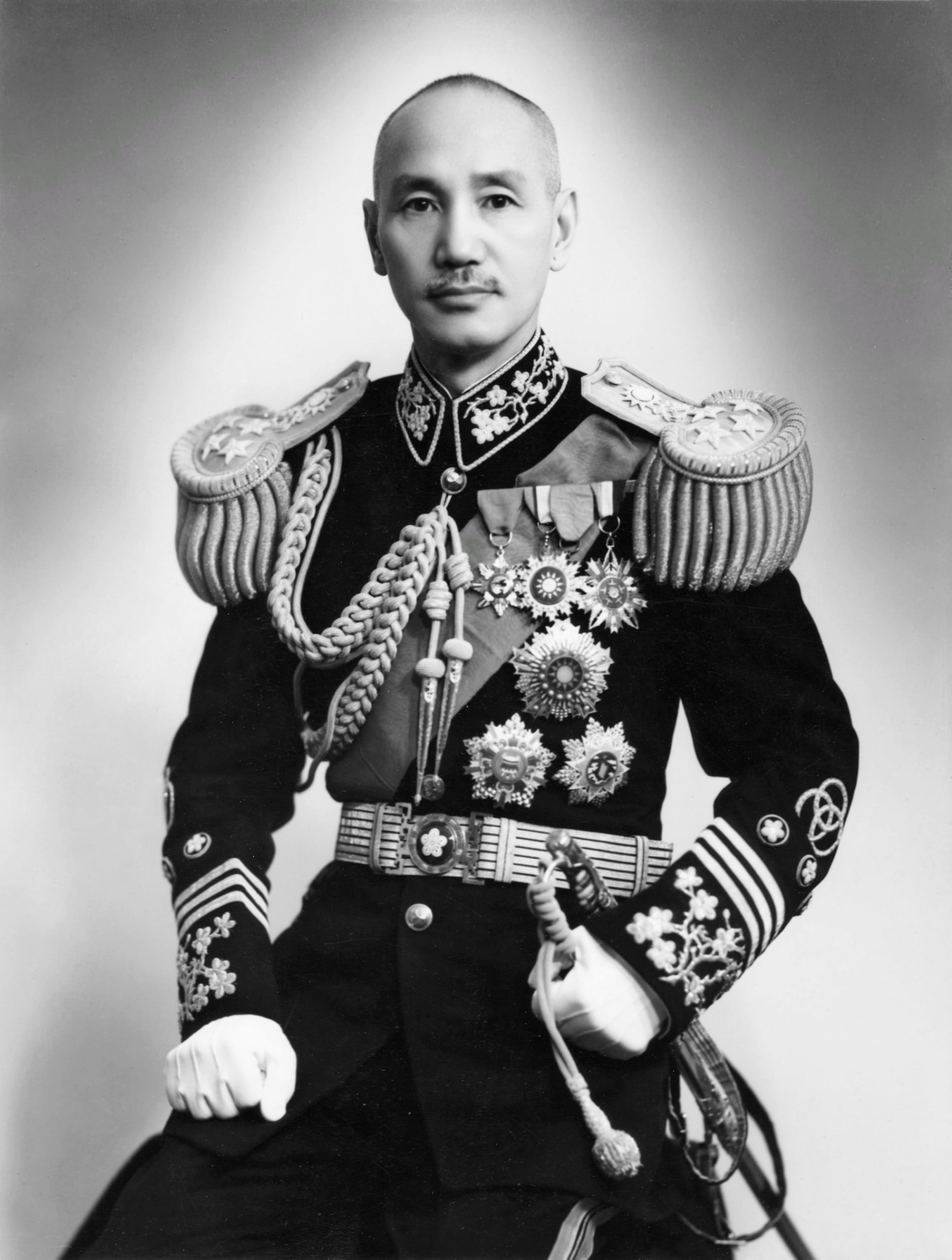Black-and-white studio portrait of an Asian military officer in ornate dress uniform, wearing medals and epaulettes, holding a ceremonial sword, facing the camera