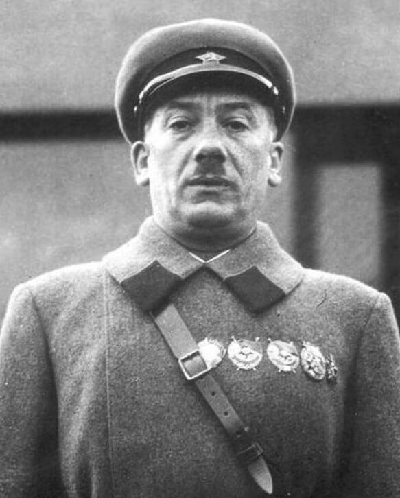 Black-and-white portrait of a stern uniformed Soviet officer, wearing a peaked cap, cross-body strap and several medals pinned to his coat