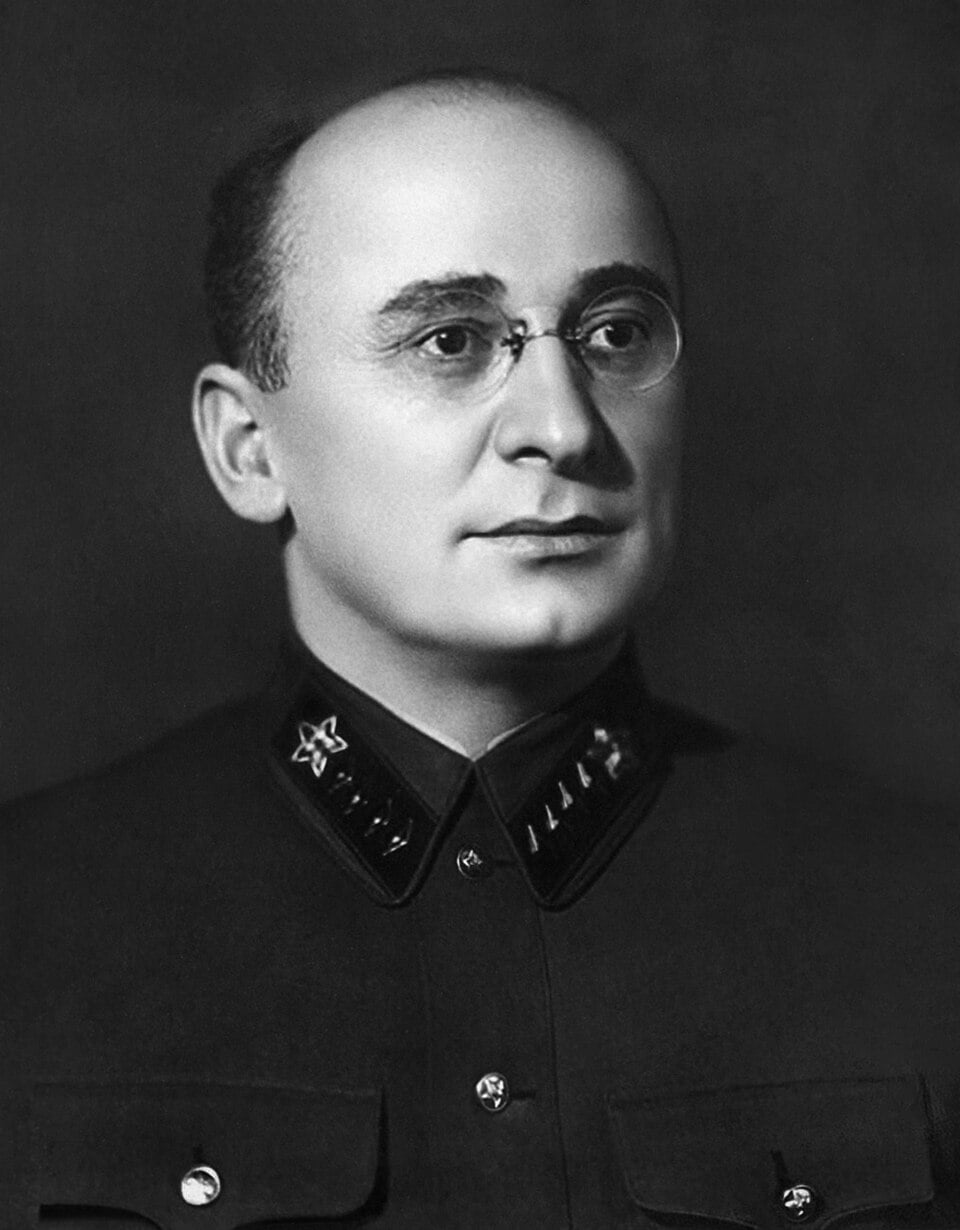 Black-and-white portrait of a stern, bespectacled man in a high-collared military uniform with star insignia, gazing slightly to the viewer’s right