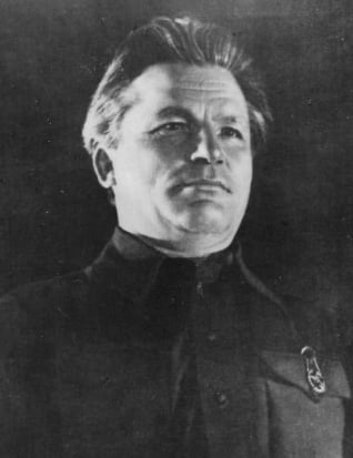 Black-and-white portrait of a middle-aged man in a dark uniform, looking slightly upward with a serious expression against a plain dark background