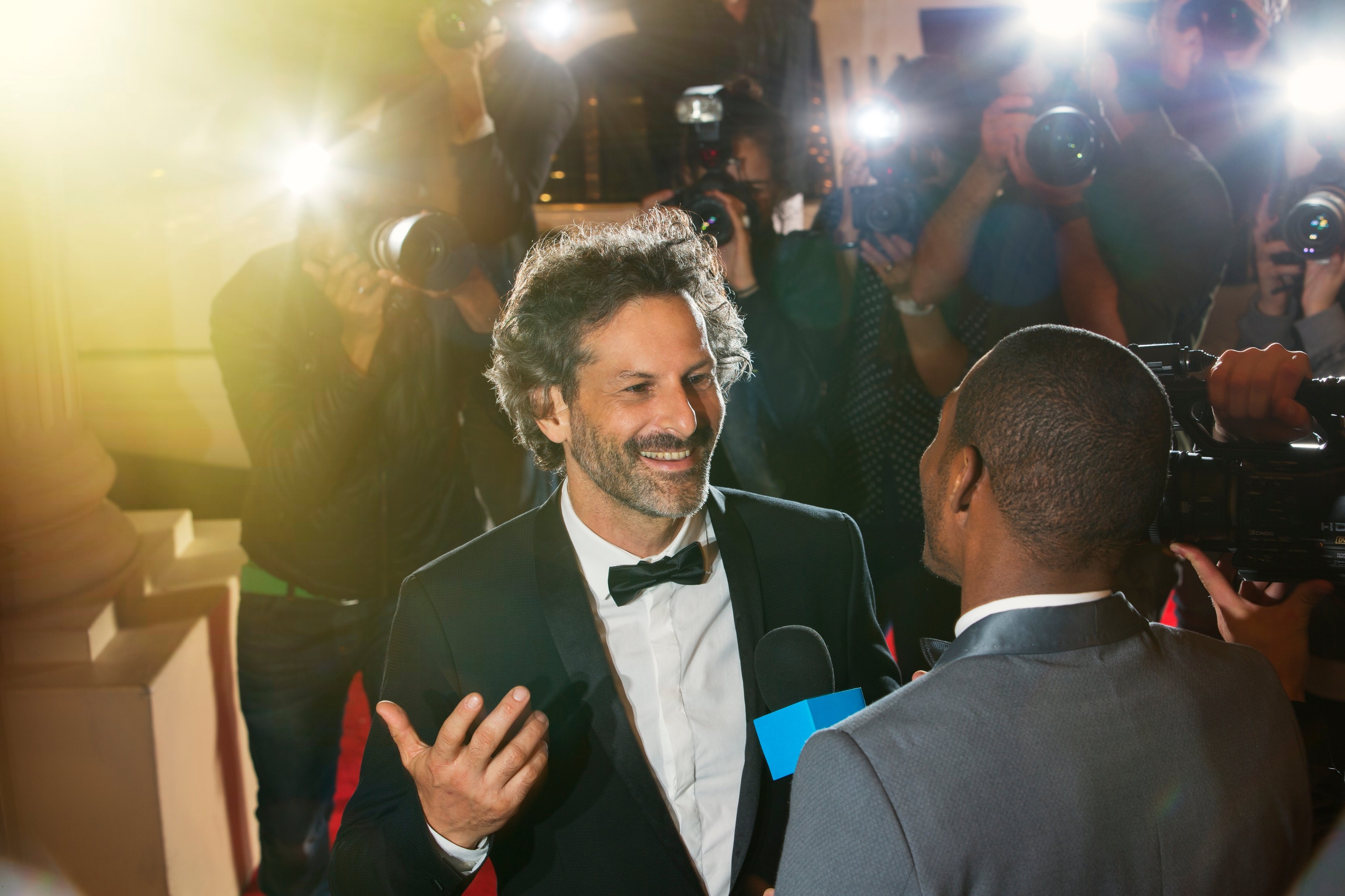 Photo 2 — Celebrity/being famous scene:
A realistic illustration showing a performer or public figure (approximately 20–30 years old) on a stage or at a public event — for example a singer performing, an actor on a red carpet, or an athlete celebrating
Cameras or photographers visible in the background to convey the public nature of fame
The celebrity figure looks confident and successful
Setting: a stage, event venue or public appearance — bright lights, crowd in background
Overall tone: glamorous but also slightly overwhelming — should prompt discussion of both advantages and disadvantages of fame
No real celebrity likenesses, brand names or logos
