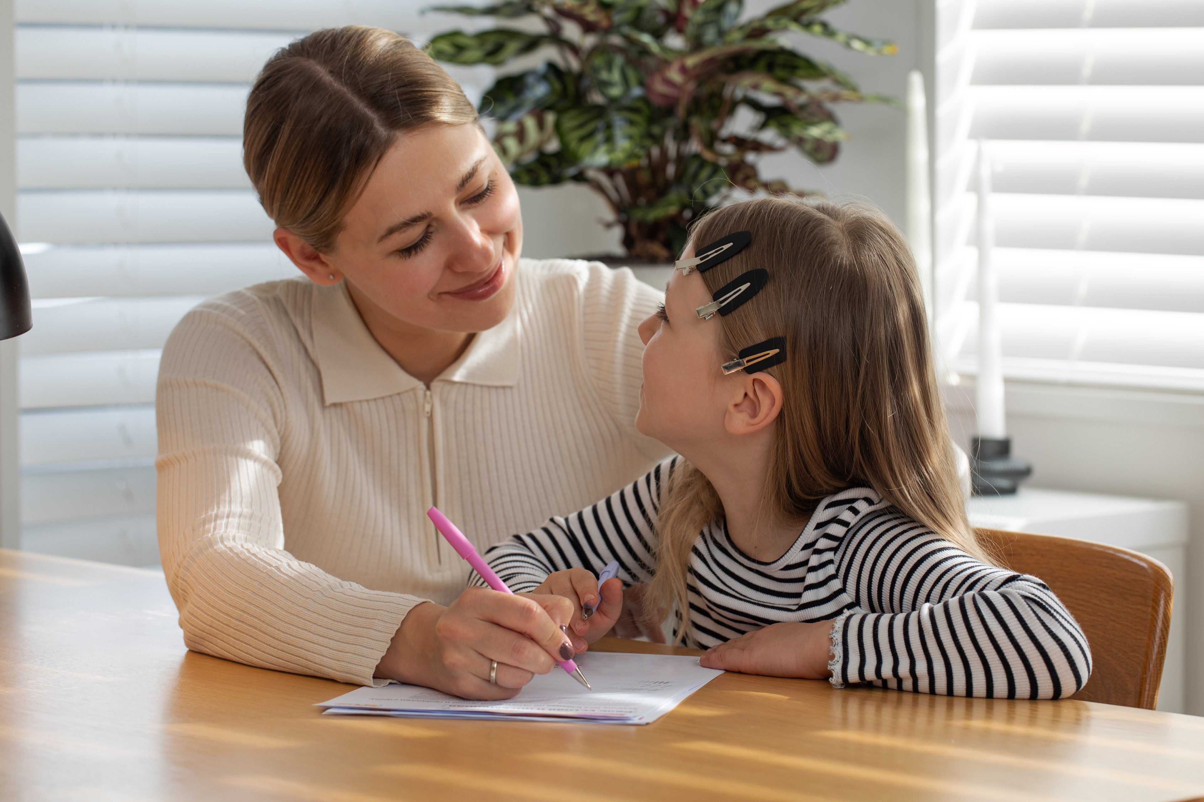 Photo 1 — Role model scene:
A warm, realistic illustration showing an adult (approximately 35–40 years old, casually dressed) sitting beside a child or young person (approximately 10–14 years old) at a table or desk
The adult is pointing at something — a book, paper, or screen — appearing to explain, guide or mentor
Both figures look engaged and positive; the adult's expression is calm, patient and encouraging
Setting: home or informal learning environment — natural light, simple background
Overall tone: warm, supportive, mentoring — conveying a positive role model relationship
No text, brand names or identifiable locations visible
Both figures should have neutral, non-specific ethnicities