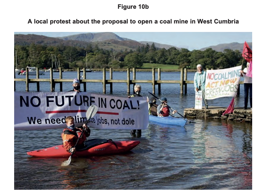 Kayakers and lakeside protesters in West Cumbria hold banners reading “No future in coal” and “No coal mine, act now, green jobs” against a rural backdrop