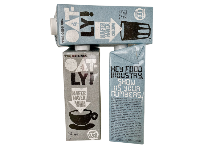 Three Oatly oat drink cartons arranged upright and sideways, showing grey and blue packaging with bold typography and a black coffee cup illustration
