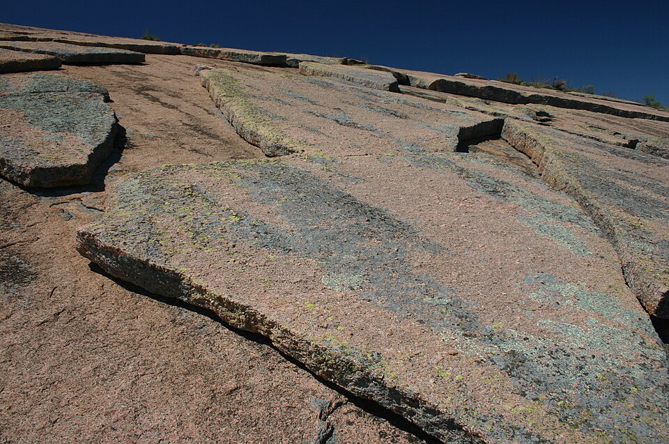 Close-up of a steep granite rock face with large cracked slabs and lichen patches under a clear deep blue sky
