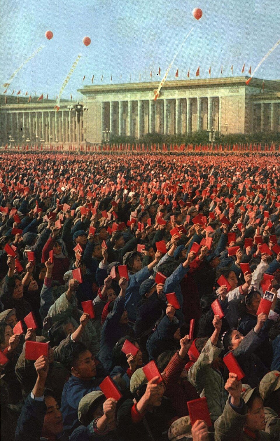 Vast crowd in Tiananmen Square raising red books before a grand government building, with red flags, balloons and banners filling the clear sky