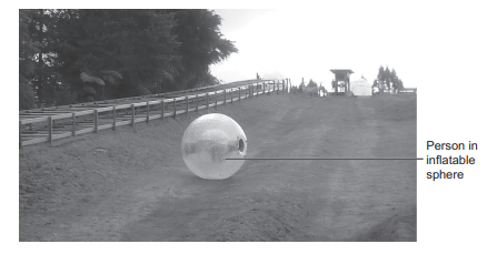 Person inside a large transparent inflatable sphere rolling down a sloping outdoor track with trees and railings in the background
