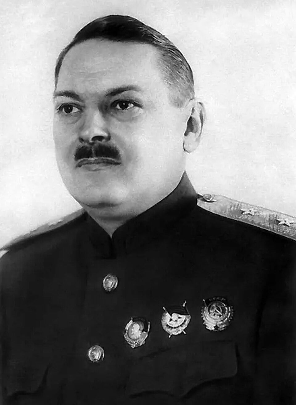Black-and-white portrait of a stern middle-aged military officer in decorated uniform, with short slicked hair and moustache, facing slightly left.