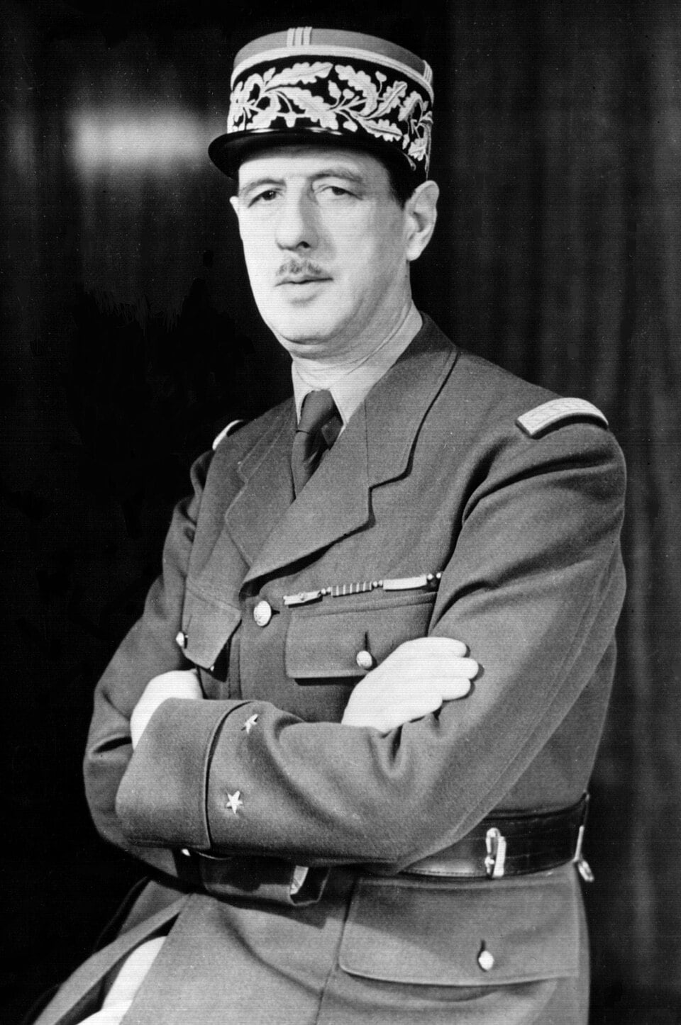 Black-and-white portrait of Charles de Gaulle in French army uniform and peaked cap, arms folded