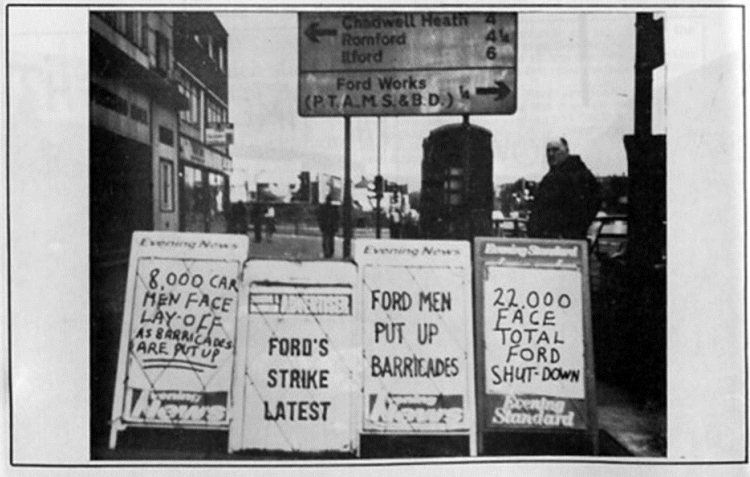 Black and white street scene with newspaper boards reporting Ford car workers’ strike, lay-offs, barricades and possible total factory shutdown