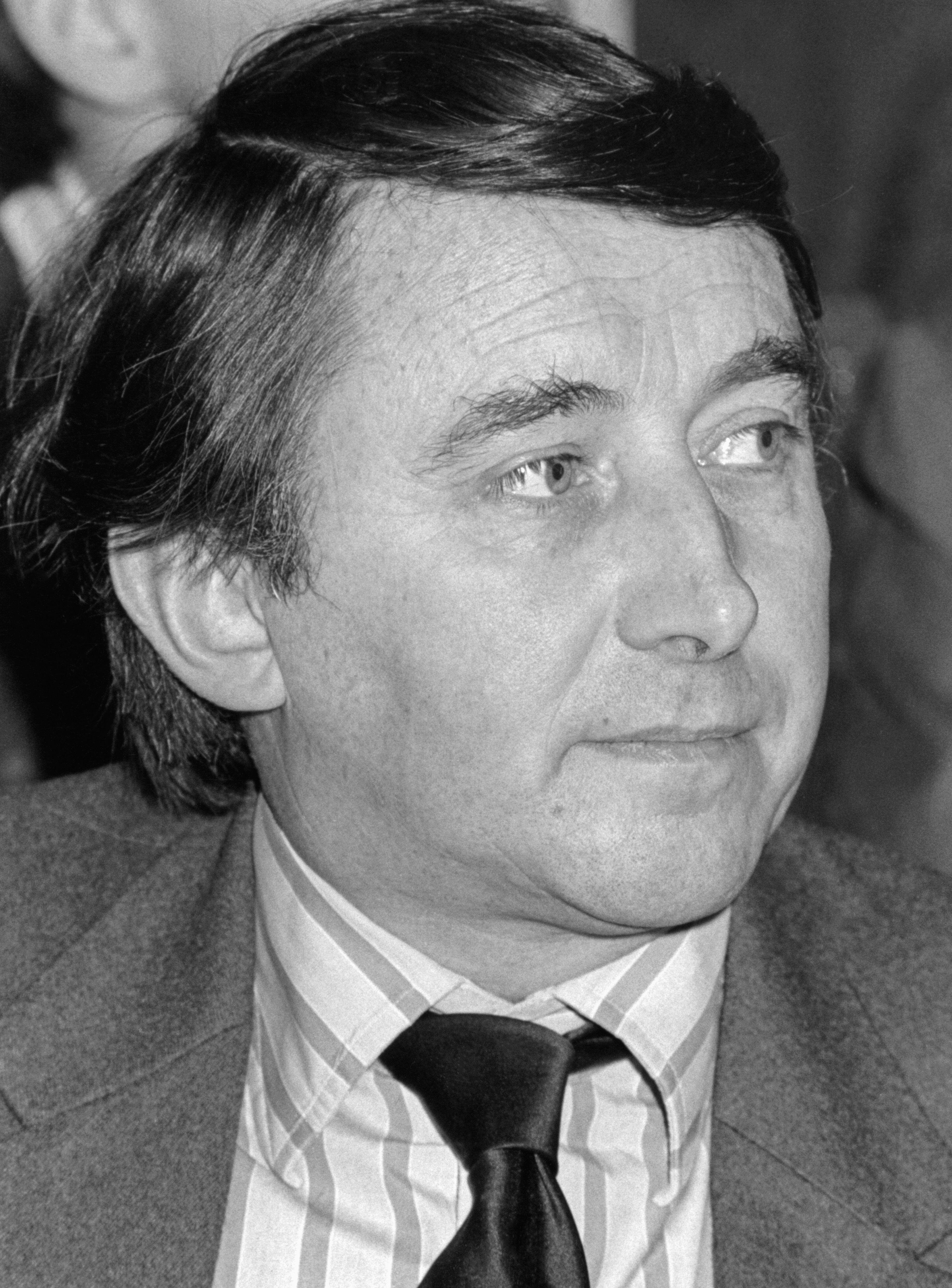A man in a black and white photograph staring forwards with a backdrop of books, David Steel