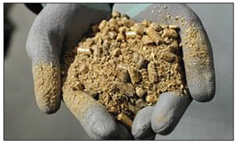 Photograph of grey-gloved hands holding a mound of coarse, beige-brown granular material, representing the refined carbon-emissions product used to make sodium hydrogencarbonate, or baking soda.