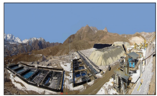 Photograph of a mountainous mining site with snow-covered ground, open industrial tanks or settling ponds, processing structures and pipes, and a large rocky spoil heap beneath a clear blue sky.