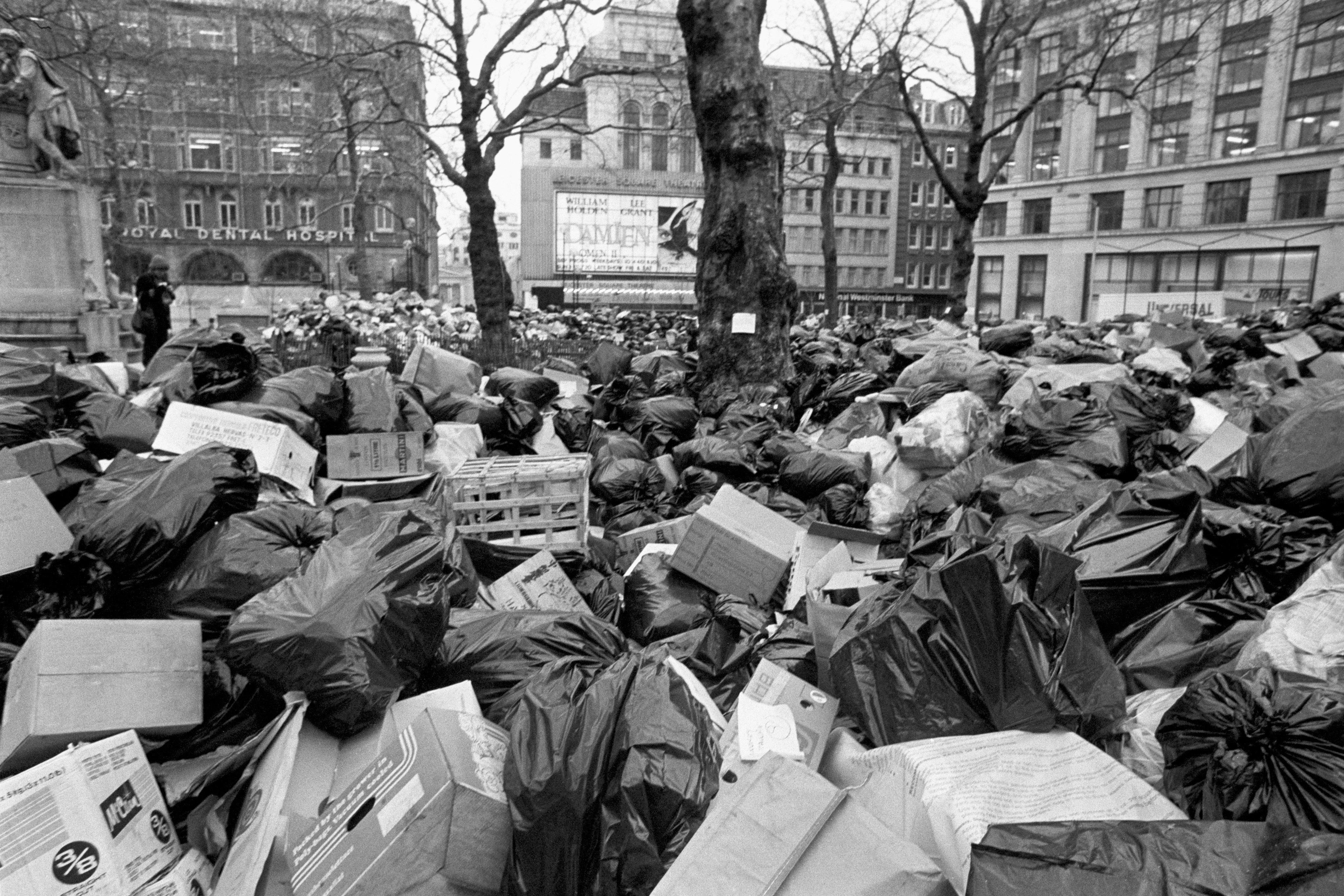 Black and white city street piled high with rubbish bags and cardboard boxes, trees and buildings in the background during a refuse workers’ strike