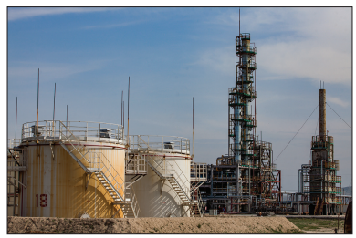Figure: Photograph of an industrial oil refinery at dusk, showing distillation towers, pipework and storage tanks illuminated by site lighting