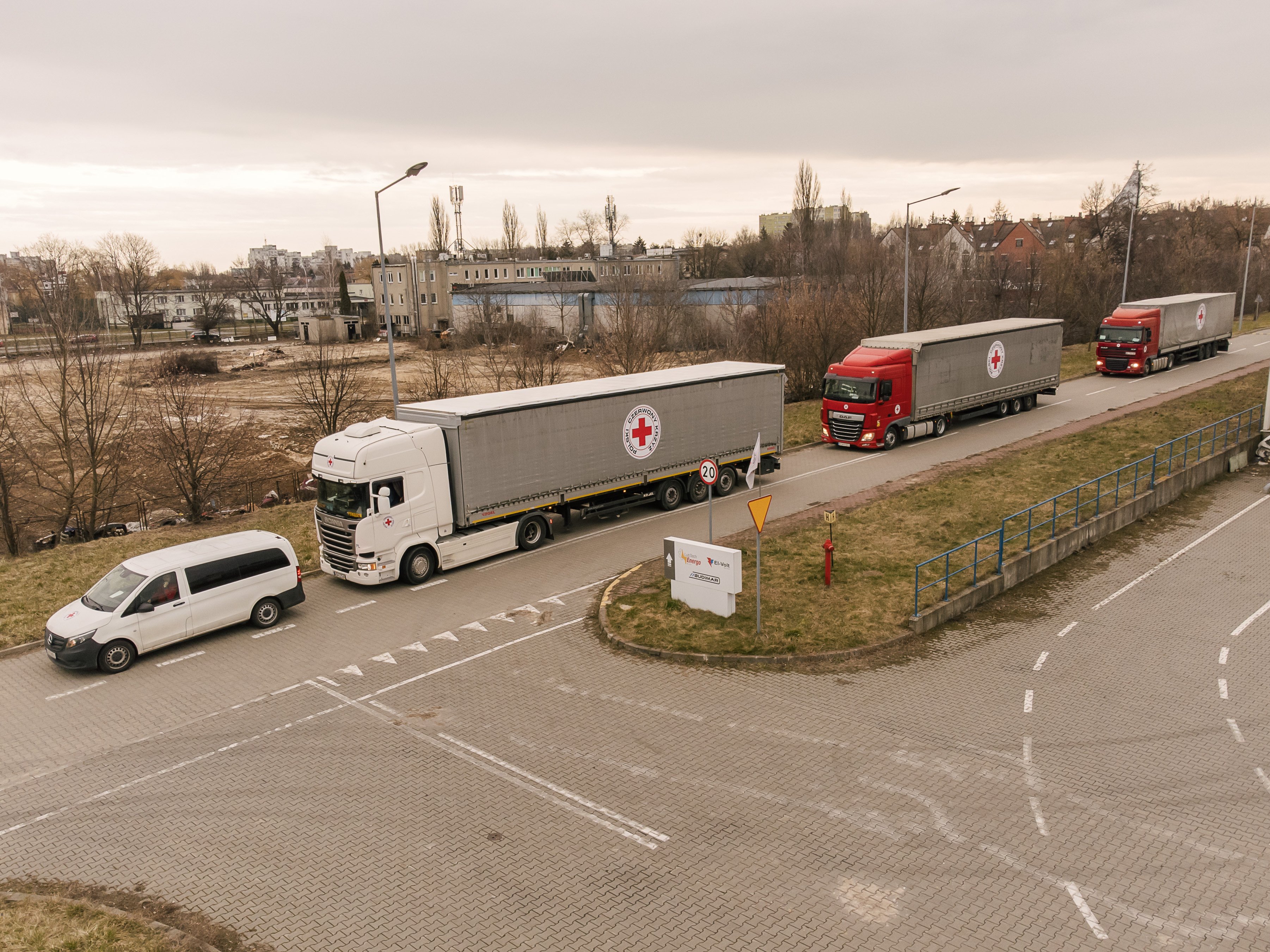 Red Cross trucks carrying humanitarian supplies travel in convoy through an urban area, illustrating the delivery of aid to civilians affected by the conflict in Ukraine.