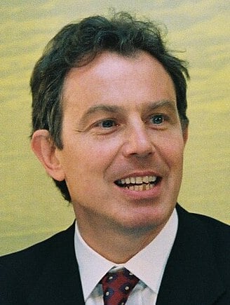 Photograph of Tony Blair, showing him smiling in a dark suit, white shirt and patterned tie.