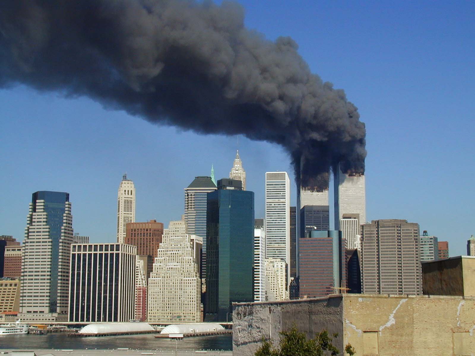 Photograph of the New York City skyline on 11 September 2001, showing both World Trade Center towers burning and producing thick black smoke after being struck by hijacked aeroplanes.