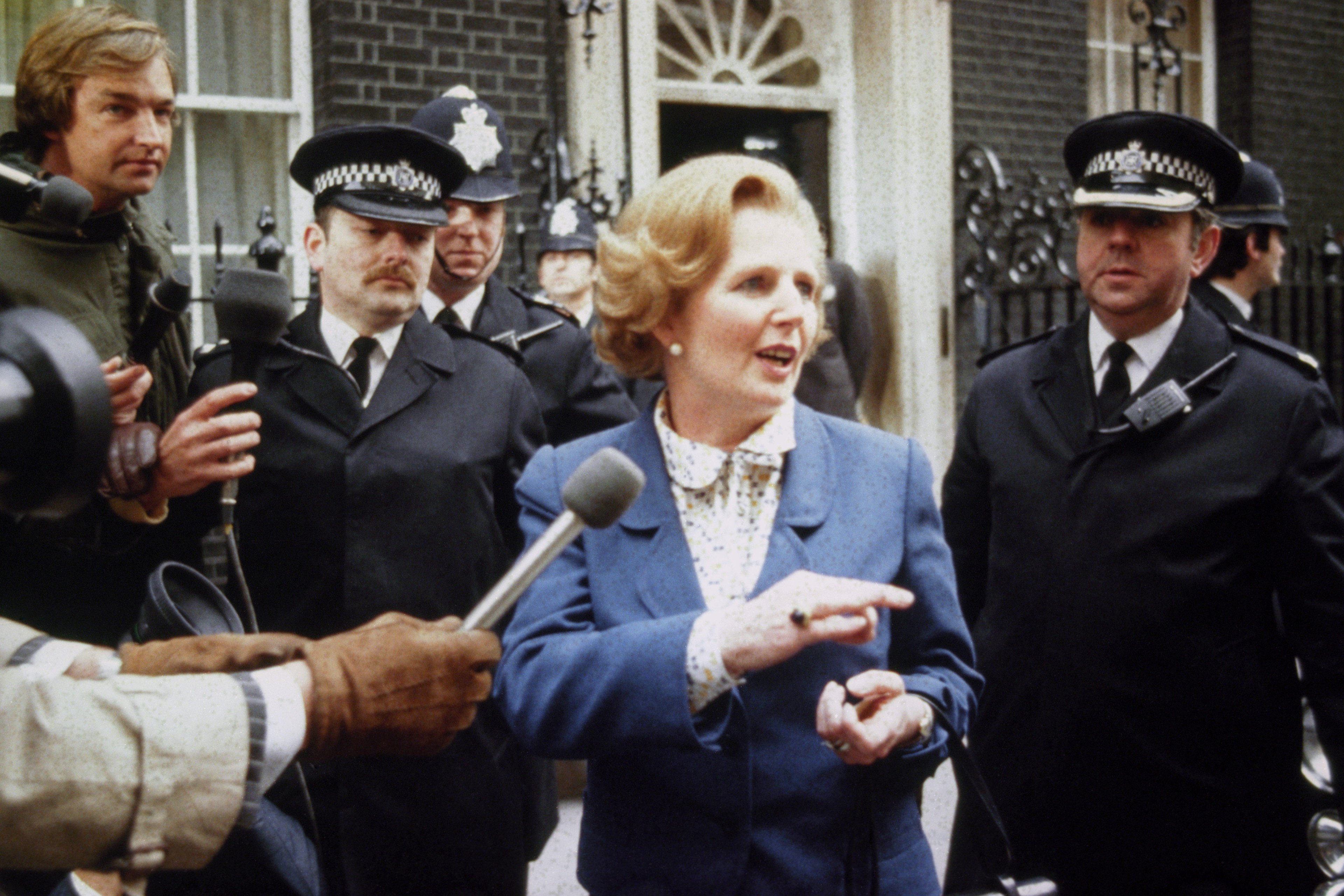 Photograph of Margaret Thatcher in a blue coat, surrounded by police officers and journalists outside the Grand Hotel in Brighton after the IRA bombing during the 1984 Conservative Party Conference.