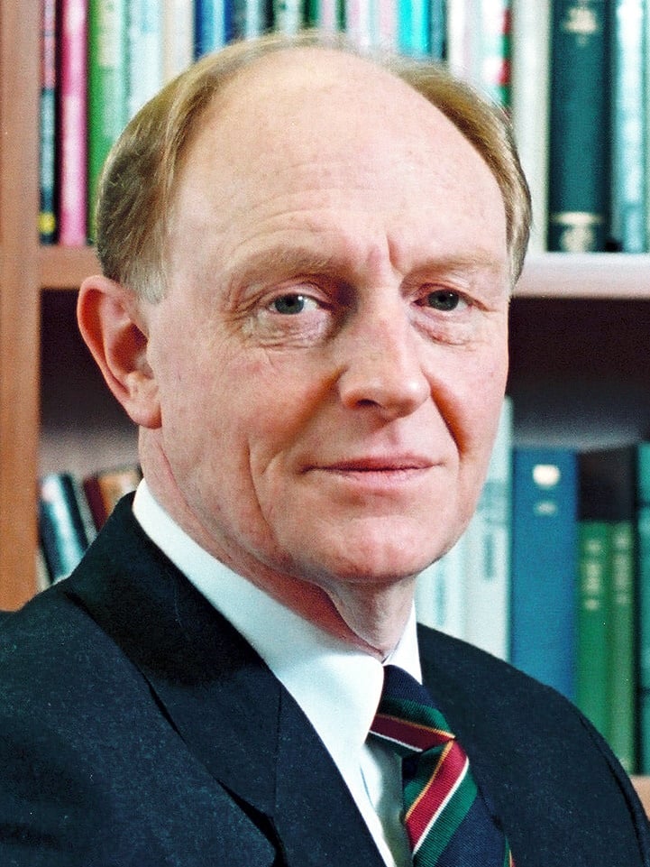 Portrait of John Smith, Labour Party leader from 1992 to 1994, wearing a dark suit, white shirt and striped tie, with bookshelves behind him.