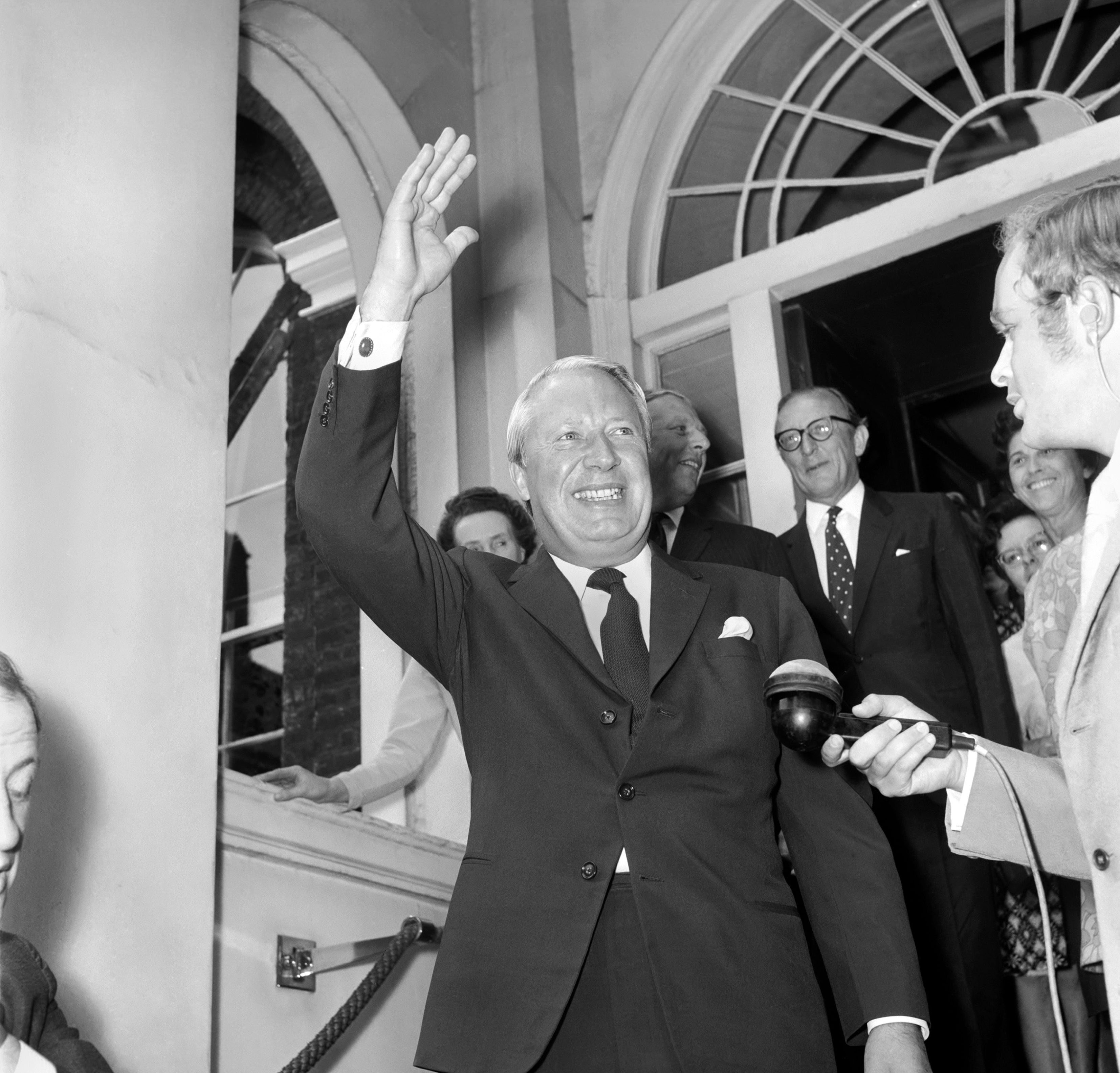Smiling man in a suit points to a large “YES” poster beside a results chart marked in percentages, suggesting support for a successful campaign